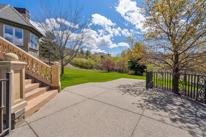 Concrete patio with decorative wrought iron fencing, stone balustrade staircase, and an expansive lawn