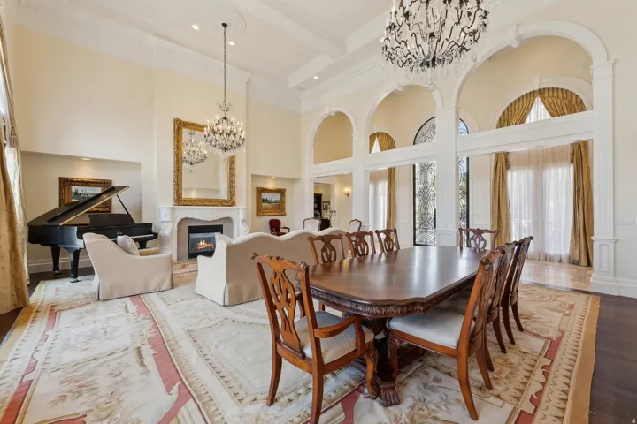 Grand great room featuring high ceilings, multiple chandeliers, arched doorways, a fireplace with a decorative mantel, and wood-finish flooring