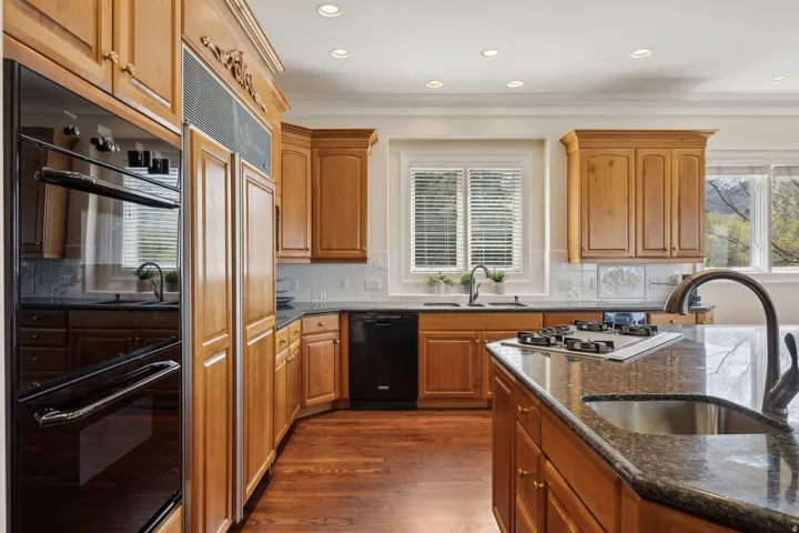 Kitchen featuring wood cabinetry, dark countertops, a built-in double oven, a center island with a gas cooktop, and recessed lighting