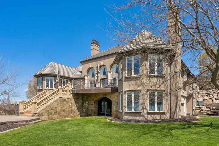 Expansive exterior featuring stucco siding, stone accents, a multi-tiered balcony, a turret with a conical roof, and an arched entry