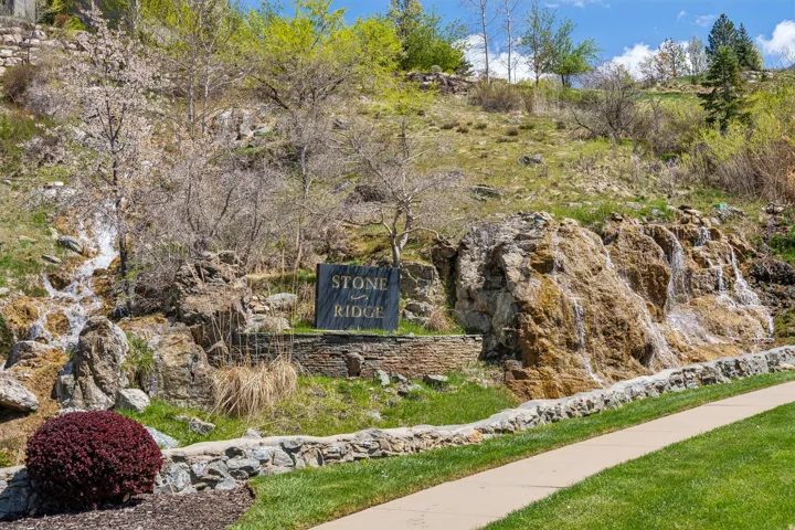 Stone Ridge sign with stone base, flanked by two cascading rock waterfalls, set against a green hillside with mature trees