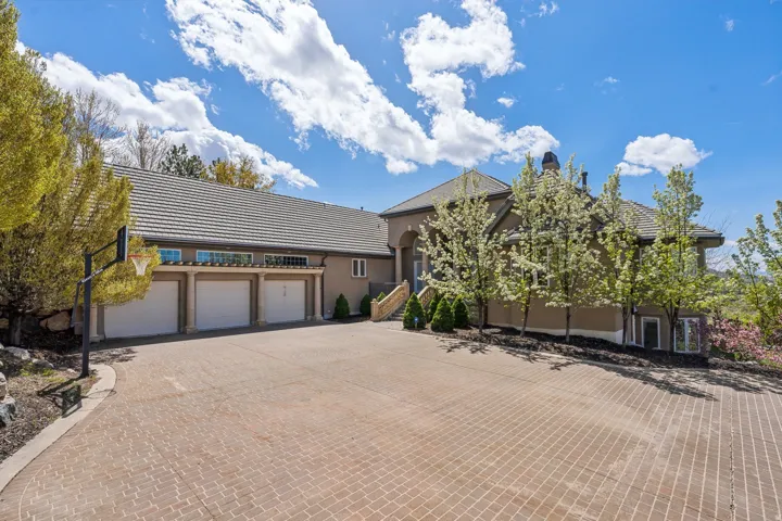 Stucco exterior with a tiled roof, multi-car garage, and a paver driveway