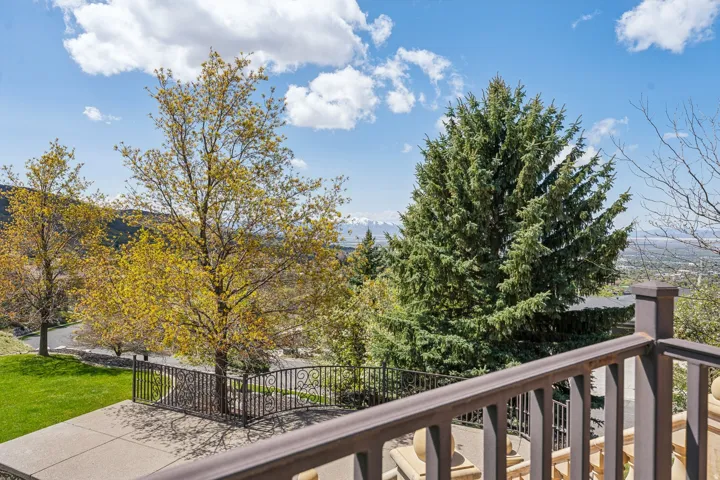 Expansive outdoor patio with decorative metal railings, mature landscaping, and distant mountain scenery