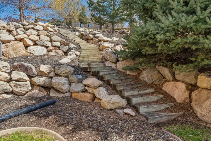 Tiered landscaping featuring natural rock retaining walls, wood-step pathway, and mature evergreen plantings