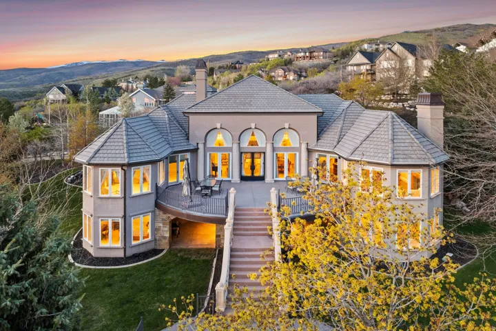 Multi-level residence featuring a gray exterior, prominent turrets, a spacious outdoor deck, and extensive exterior lighting
