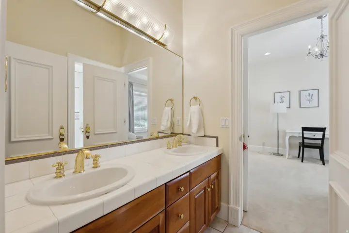 Dual vanity with brass fixtures, tile countertop, and wood-finish cabinetry