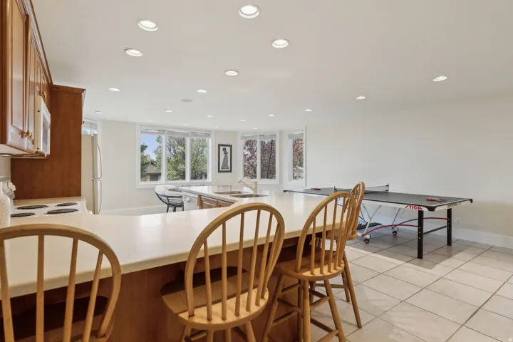 Recessed lighting illuminates an open-concept space featuring a kitchen with wood cabinetry and a peninsula with seating