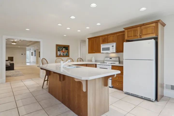 Kitchen featuring wood cabinetry, white appliances, recessed lighting, and tile flooring