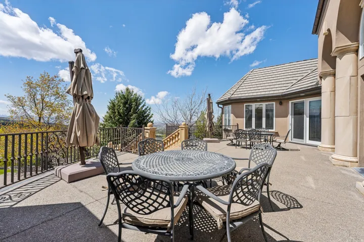 Expansive outdoor patio featuring a concrete surface, decorative metal railing, multiple sets of patio doors, and a tiled roofline