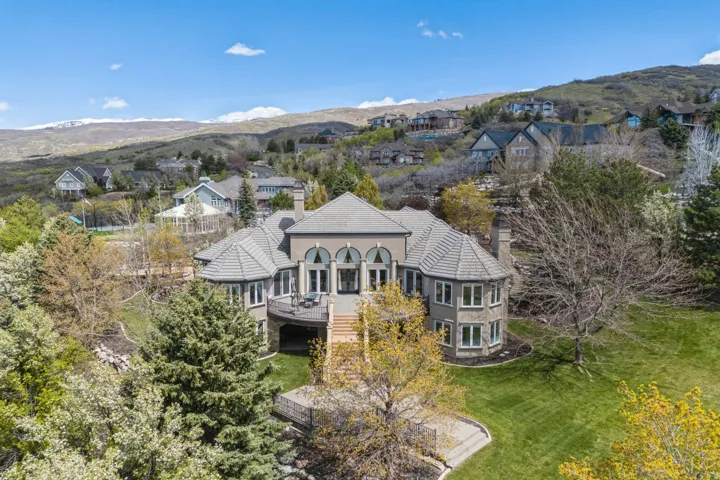 Expansive property featuring a multi-level structure, a large rear balcony, a manicured lawn, and mature trees, set against a mountainous backdrop