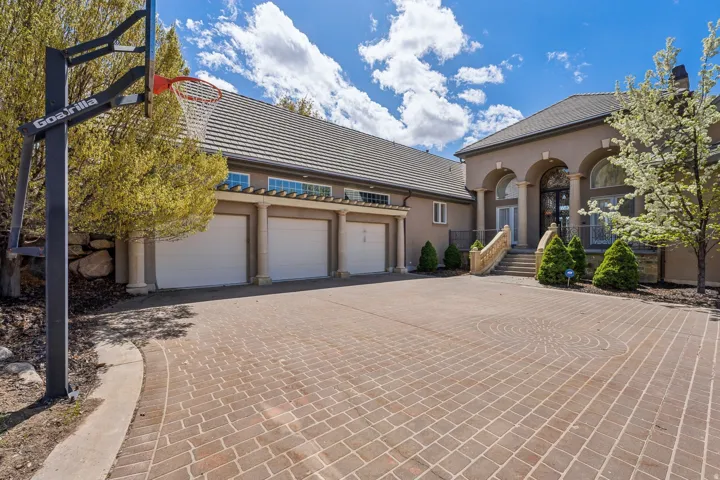 Paver driveway with decorative circular patterns, arched entry with columns, three garage bays, and a tiled roof
