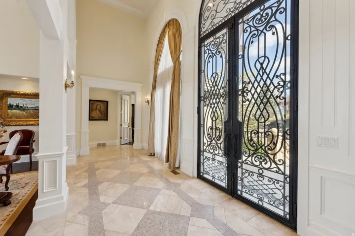Two-story entry with patterned tile flooring, wrought iron double doors, and architectural columns