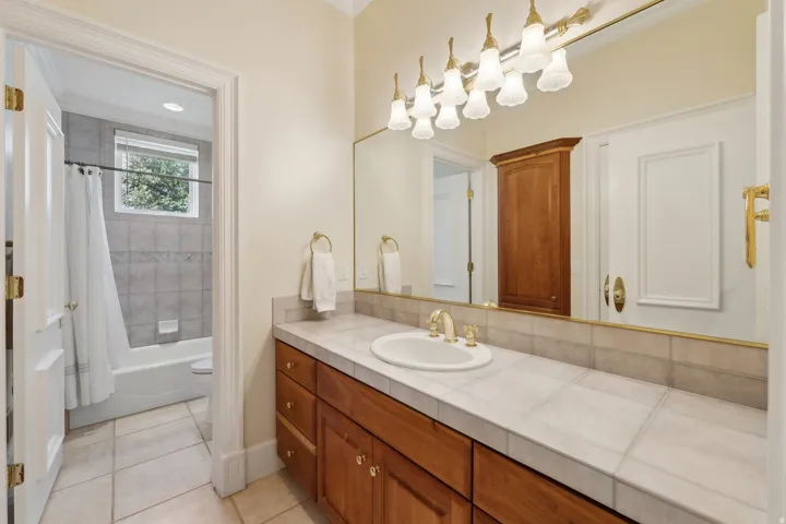 Single vanity with a tile countertop, wood-finish cabinetry, and gold-finish fixtures