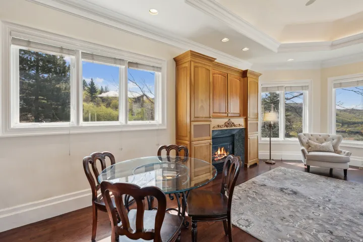Wood-finish flooring with a gas fireplace featuring a stone surround and wood cabinetry, crown molding, and large windows