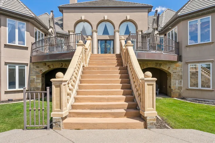 Grand exterior staircase with stone balustrades, wrought iron balcony, arched windows, and a stone archway