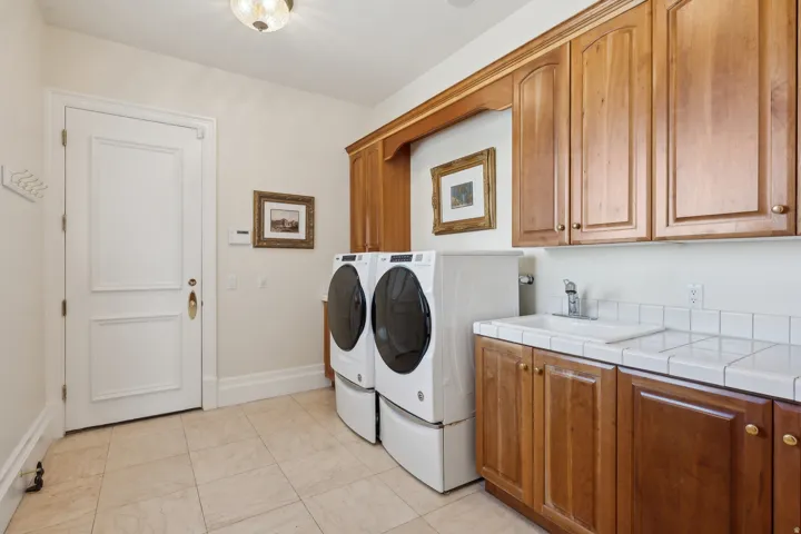 Built-in wood-finish cabinetry, tile flooring, laundry sink with tile countertop, and a panel door with brass hardware