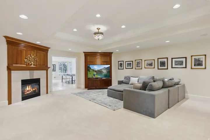 Recessed lighting, crown molding, built-in media cabinetry, and a fireplace with a stone surround and wood mantle
