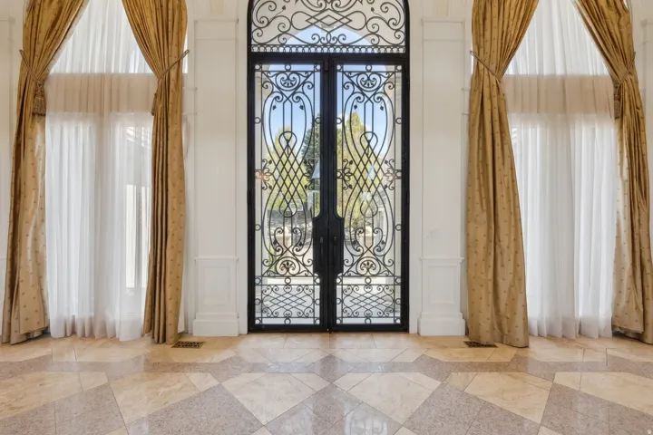 Ornate wrought iron double entry doors, flanking tall windows with arched transoms, and a patterned tile floor