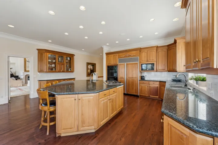 Hardwood flooring throughout, extensive wood cabinetry, dark granite countertops, recessed lighting, and a kitchen island with seating