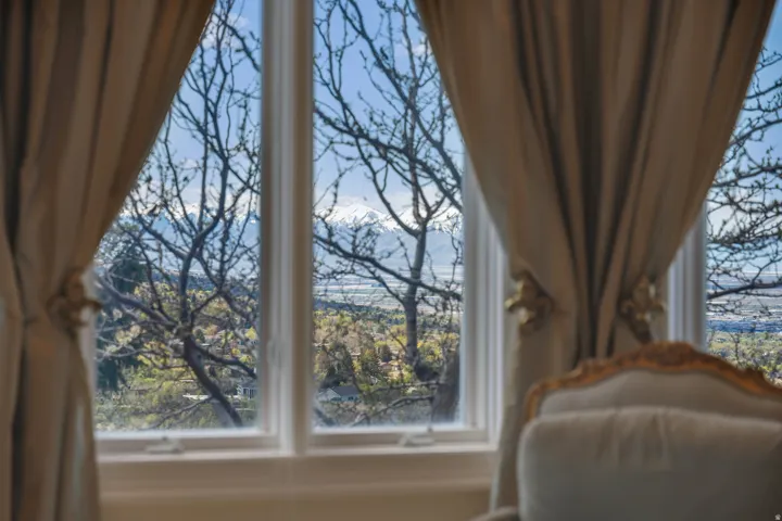 White-framed windows with decorative drapery overlooking a snow-capped mountain range and distant landscape