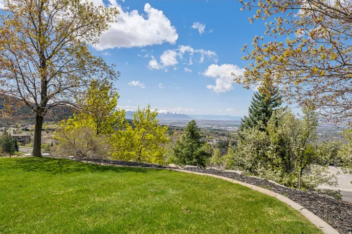 Expansive lawn area with a stone-edged planting bed, mature trees, and distant mountain scenery