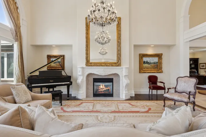 Sleek fireplace with an ornate mantel, a grand chandelier, and high ceilings with arched details