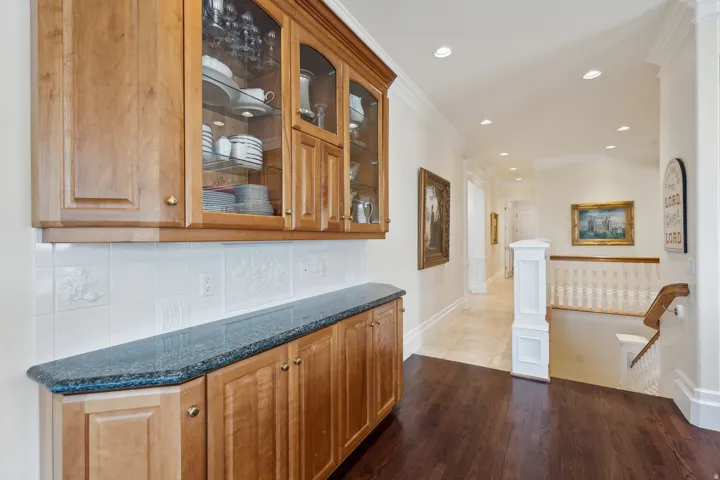 Custom built-in cabinetry with glass display fronts, dark stone countertop, white tile backsplash, wood-finish flooring, and recessed lighting