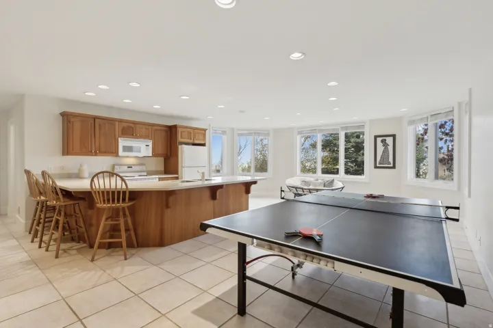Open common area featuring recessed lighting, a full kitchen with wood cabinetry and appliances, a spacious island with bar seating, and multiple bay windows