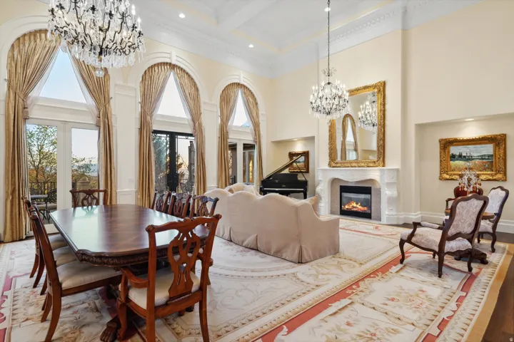 Expansive room featuring multiple arched windows, elegant chandeliers, a grand fireplace with a stone mantel, and detailed crown molding