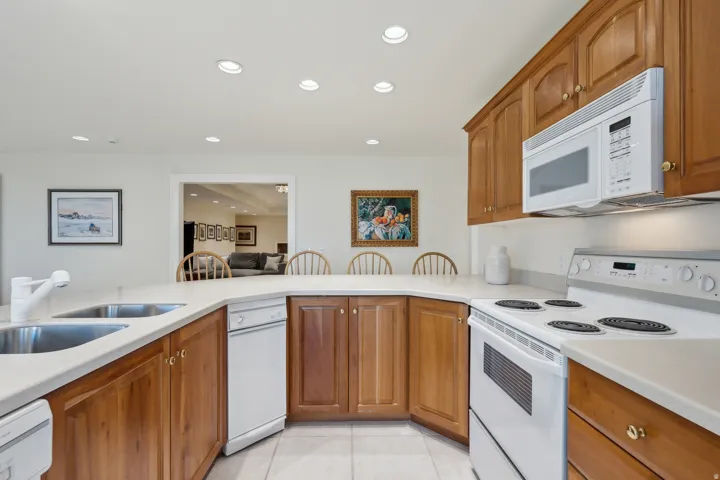Kitchen featuring wood cabinetry, white countertops, dual stainless steel sinks, a built-in microwave, and a white electric range