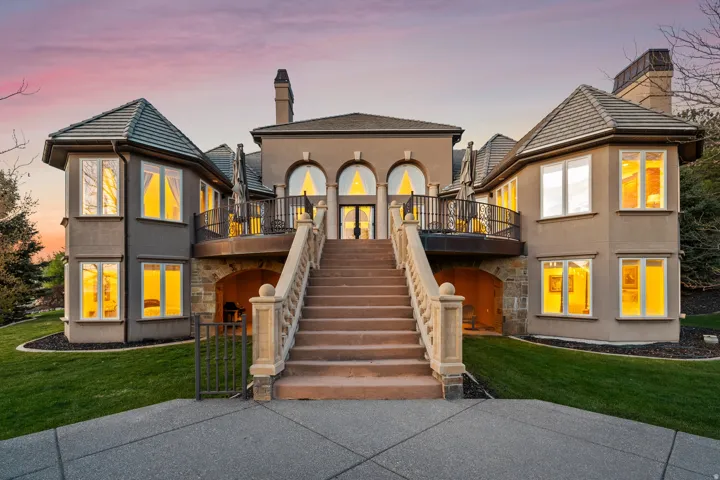 Stucco exterior featuring dual turret-style wings, a grand stone staircase, a balcony with wrought iron railing, and arched windows