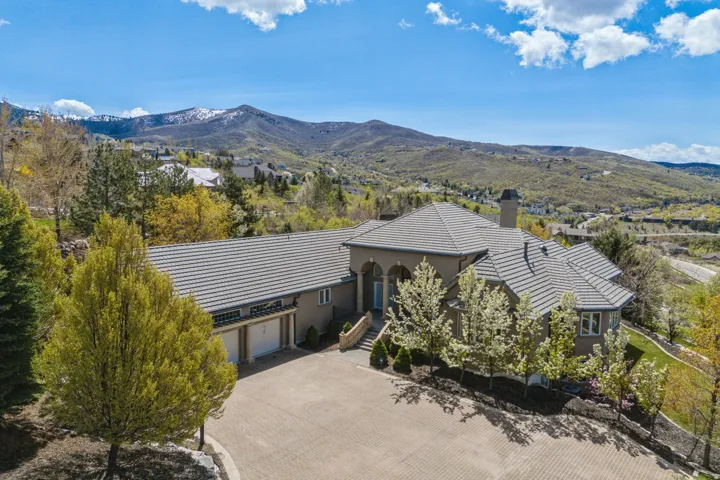 Multi-level residence featuring a tile roof, stucco exterior, and a paver driveway