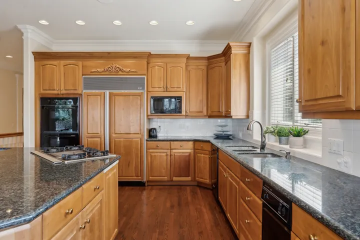 Kitchen featuring wood-finish flooring, recessed lighting, granite countertops, built-in double ovens, and a built-in refrigerator