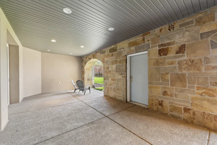 Expansive covered patio featuring a stone accent wall, arched stone entryway, recessed lighting, and a textured concrete surface