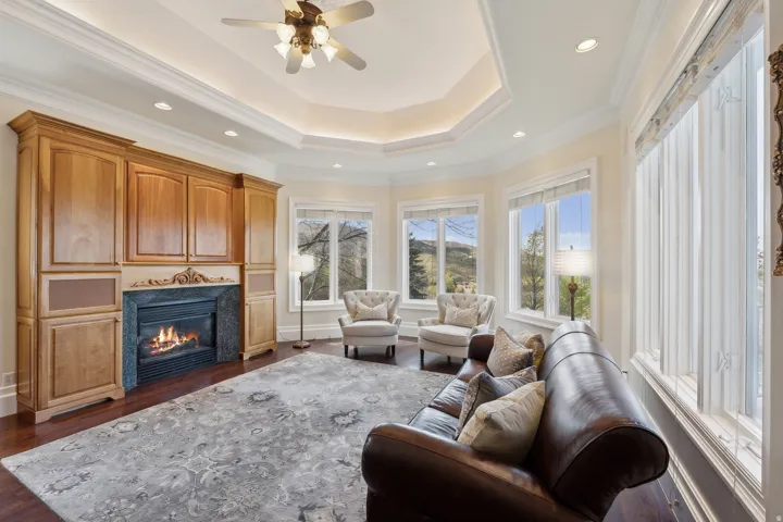 Built-in cabinetry with integrated fireplace, wood-finish flooring, multiple windows, recessed lighting, and a tray ceiling