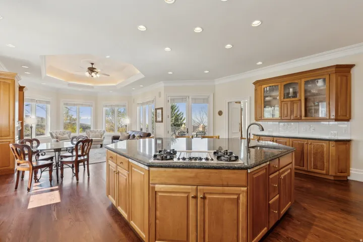 Kitchen island with cooktop and sink, wood-finish flooring, built-in cabinetry, recessed lighting, and bay windows