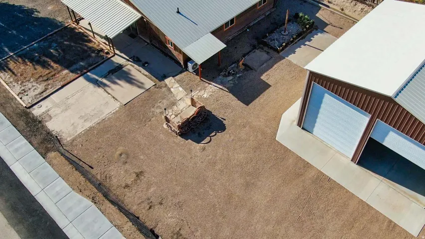 Detached metal-sided garage with two roll-up doors, gravel ground cover, concrete walkways, and a covered porch with a metal roof
