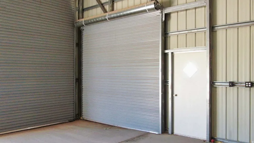 Metal structure with corrugated paneling, featuring two roll-up doors and a pedestrian door with a diamond-shaped window