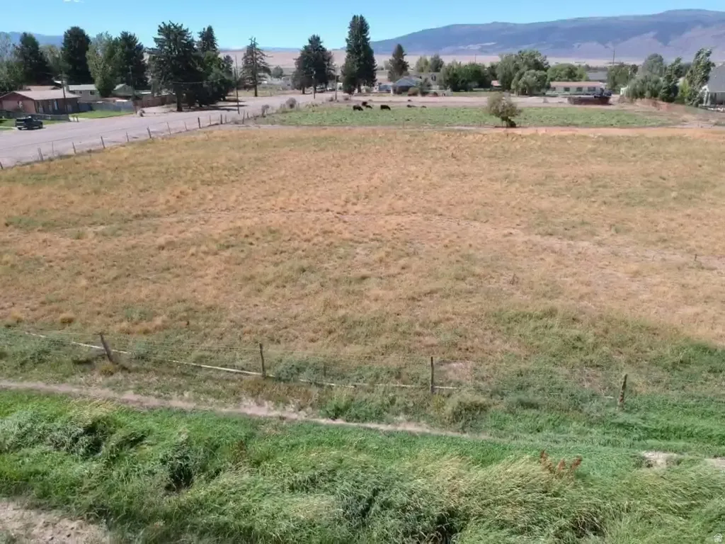 Expansive undeveloped land featuring natural grasses and perimeter fencing, with distant mountainous terrain