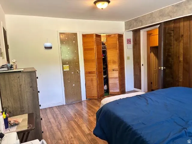 Wood-finish flooring throughout, featuring a ceiling-mounted light fixture, louvered bi-fold closet doors, and wood paneling