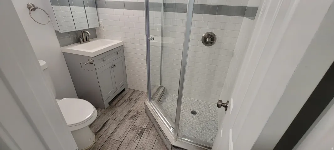 Wood-finish flooring, white subway tile walls with a gray accent band, and a glass-enclosed shower with a pebble-style floor