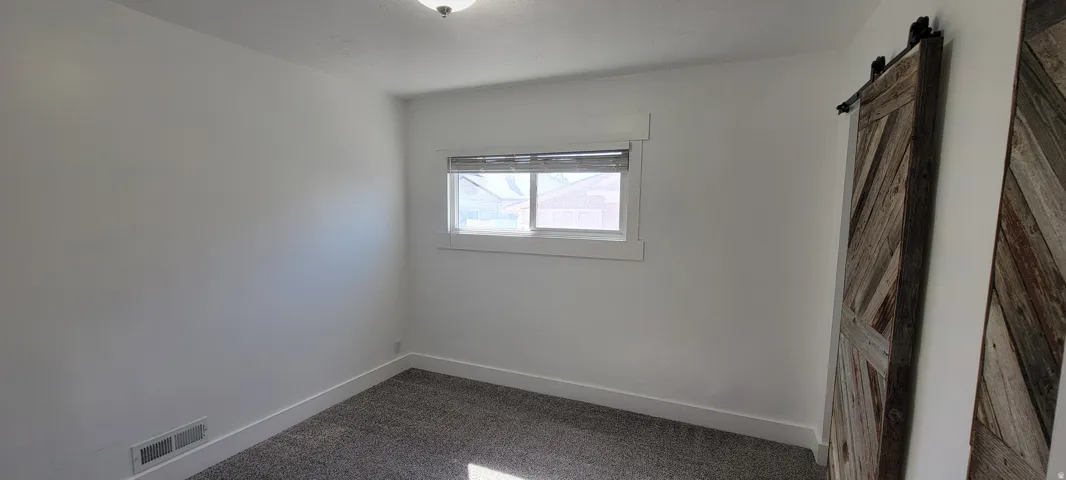 White painted walls with carpeted flooring, featuring a window with blinds and a barn door with a chevron pattern