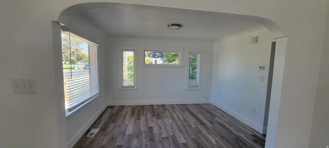 Wood-finish flooring with white baseboards, featuring multiple windows with blinds, a flush mount ceiling light, and an arched entryway