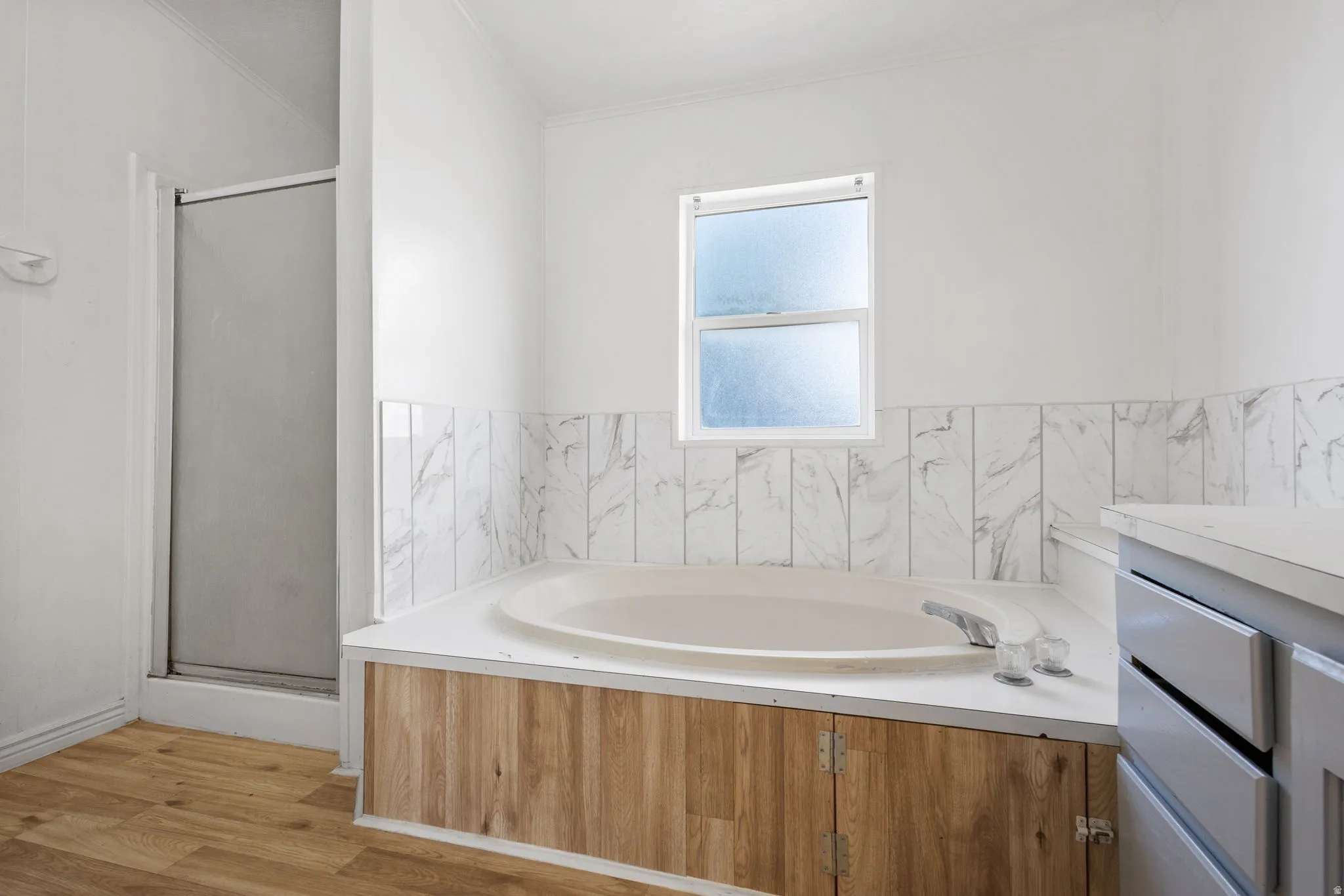 Built-in bathtub with a wood-finish surround, a shower enclosure, wood-finish flooring, and a window