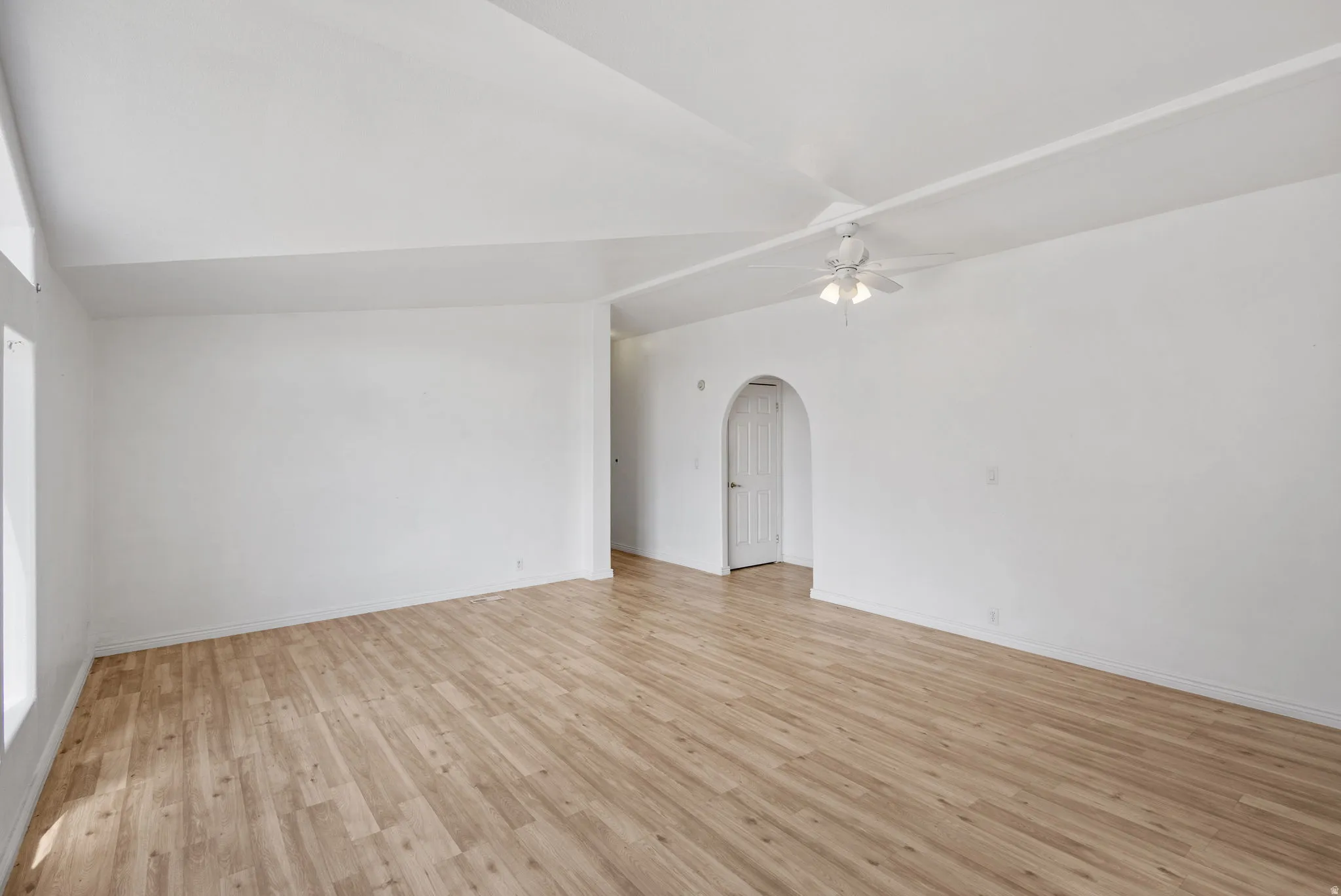 Vaulted ceiling with a ceiling fan, wood-finish flooring, and an arched doorway