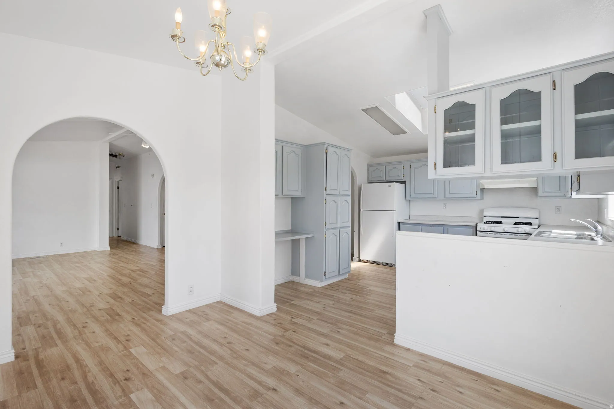Open-concept living area featuring wood-finish flooring, arched doorways, a chandelier, and a kitchen with light blue cabinetry and a skylight