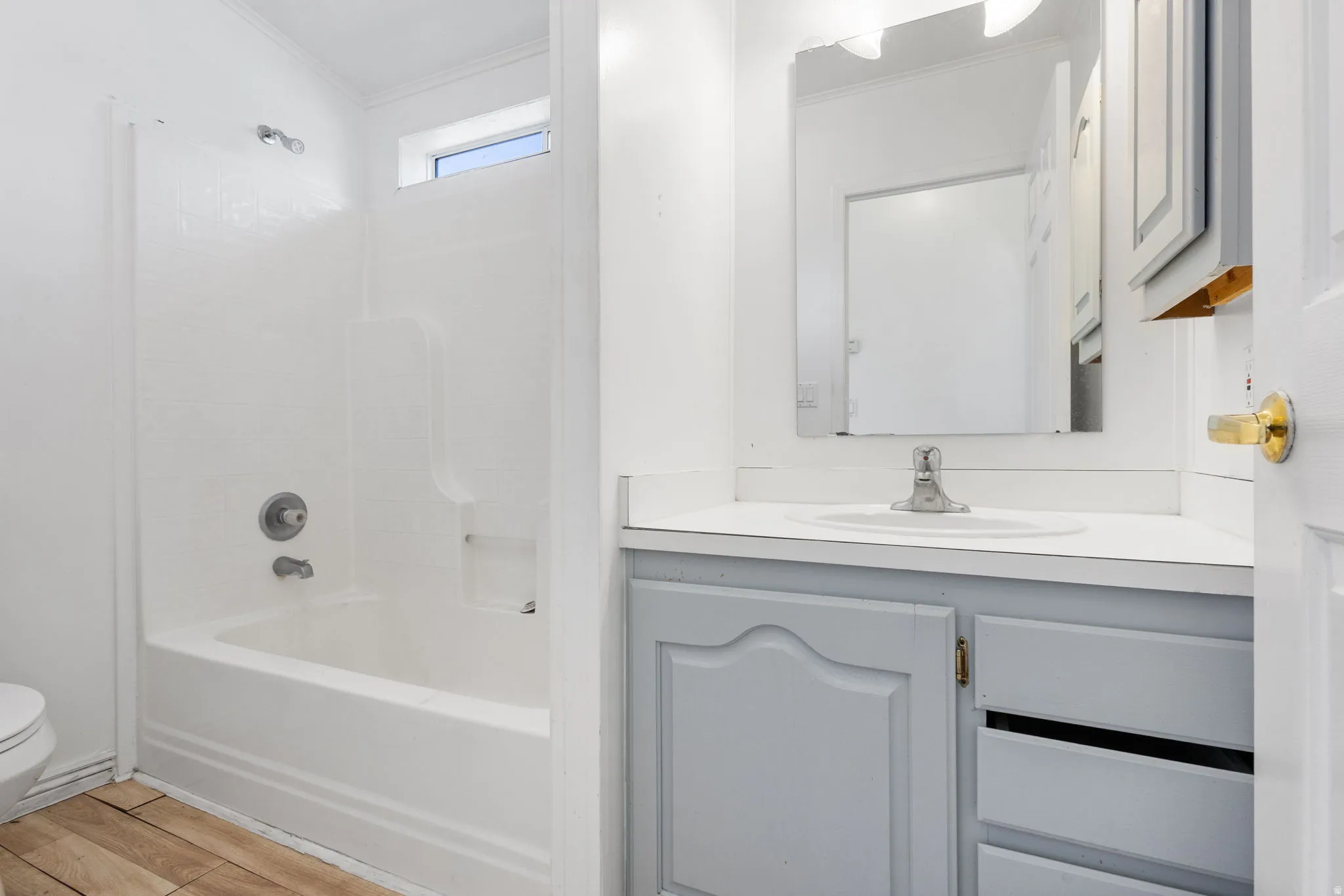 White vanity with integrated sink, wood-finish flooring, white tub and shower combination, and an upper transom window