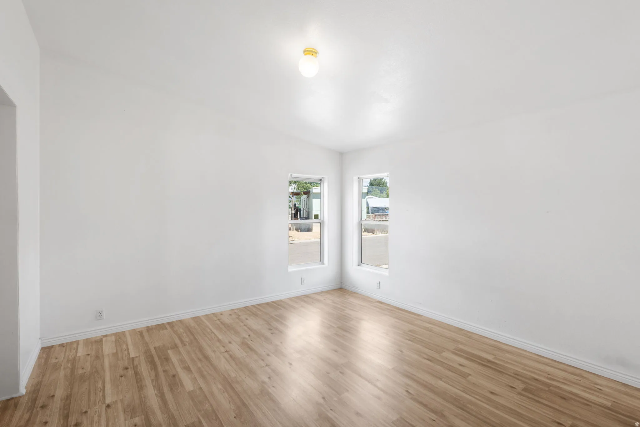 Vaulted ceiling, two windows, wood-finish flooring, white walls, and a ceiling-mounted light fixture