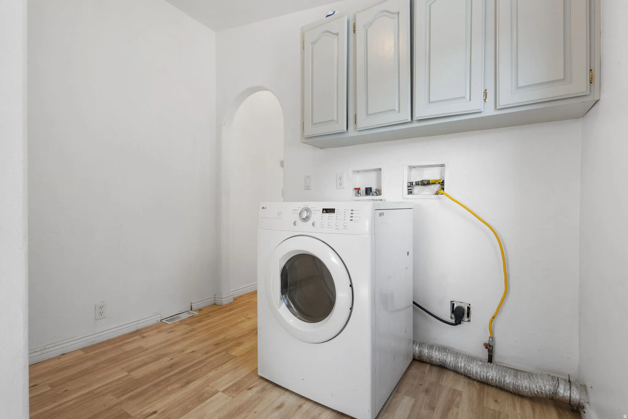 Laundry space featuring wood-finish flooring, overhead cabinetry, and an arched doorway