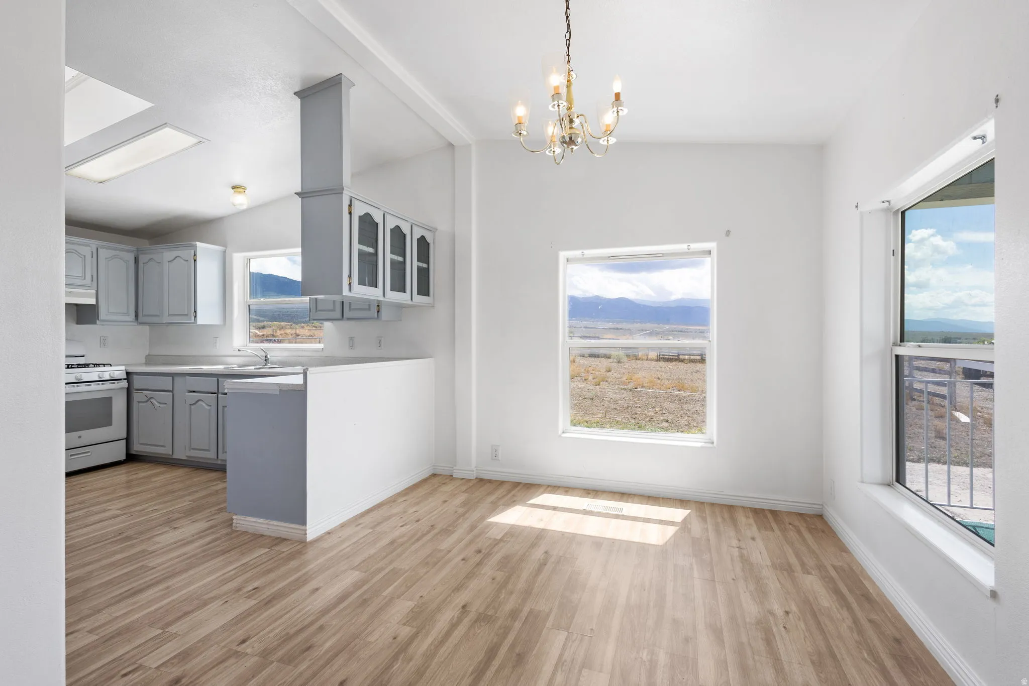 Open-concept layout featuring wood-finish flooring, a kitchen with gray cabinetry and white appliances, and an adjacent dining area with a chandelier